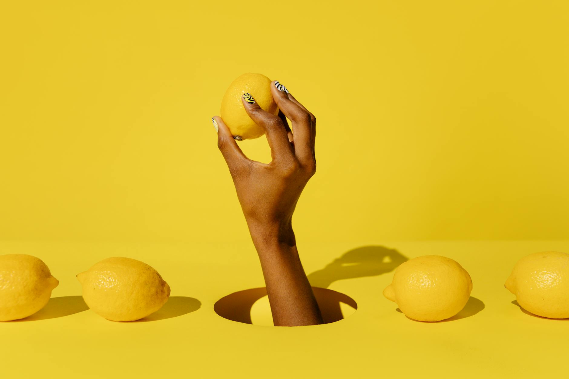 A hand holding a fresh lemon against a vivid yellow background, representing reconnection and renewal