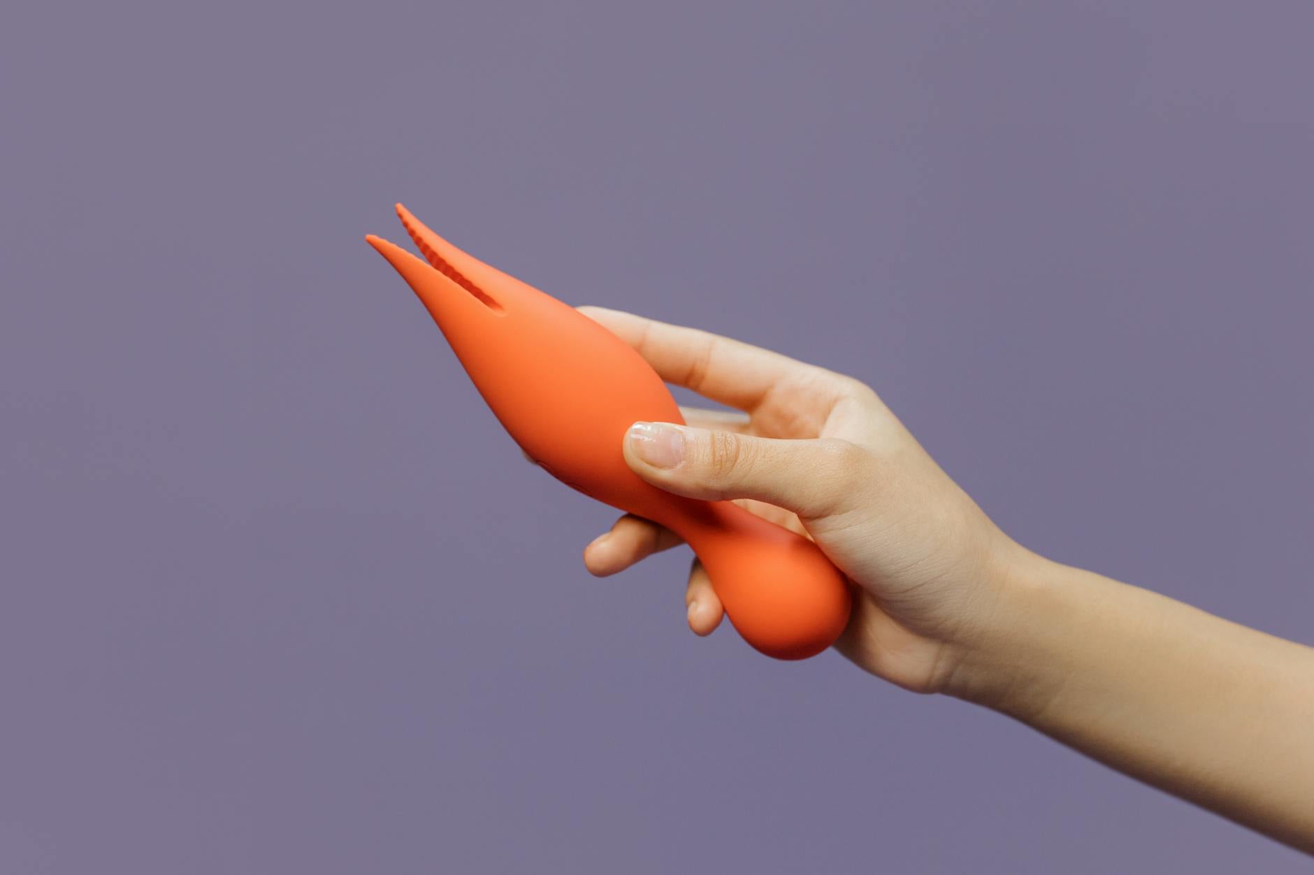 Close-up of a hand holding a bright vibrator against a minimalist purple backdrop, representing modern intimate pleasure.