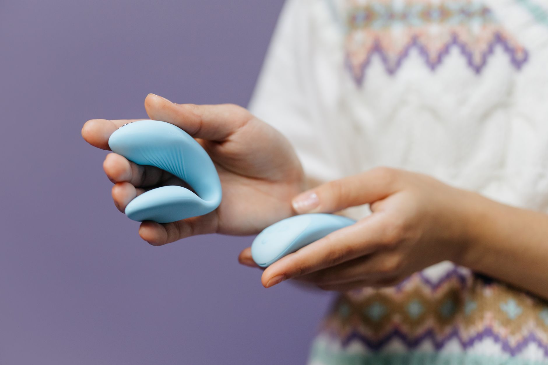 Hands holding a sleek blue clitoral vibrator, symbolizing intimate wellness adjustments