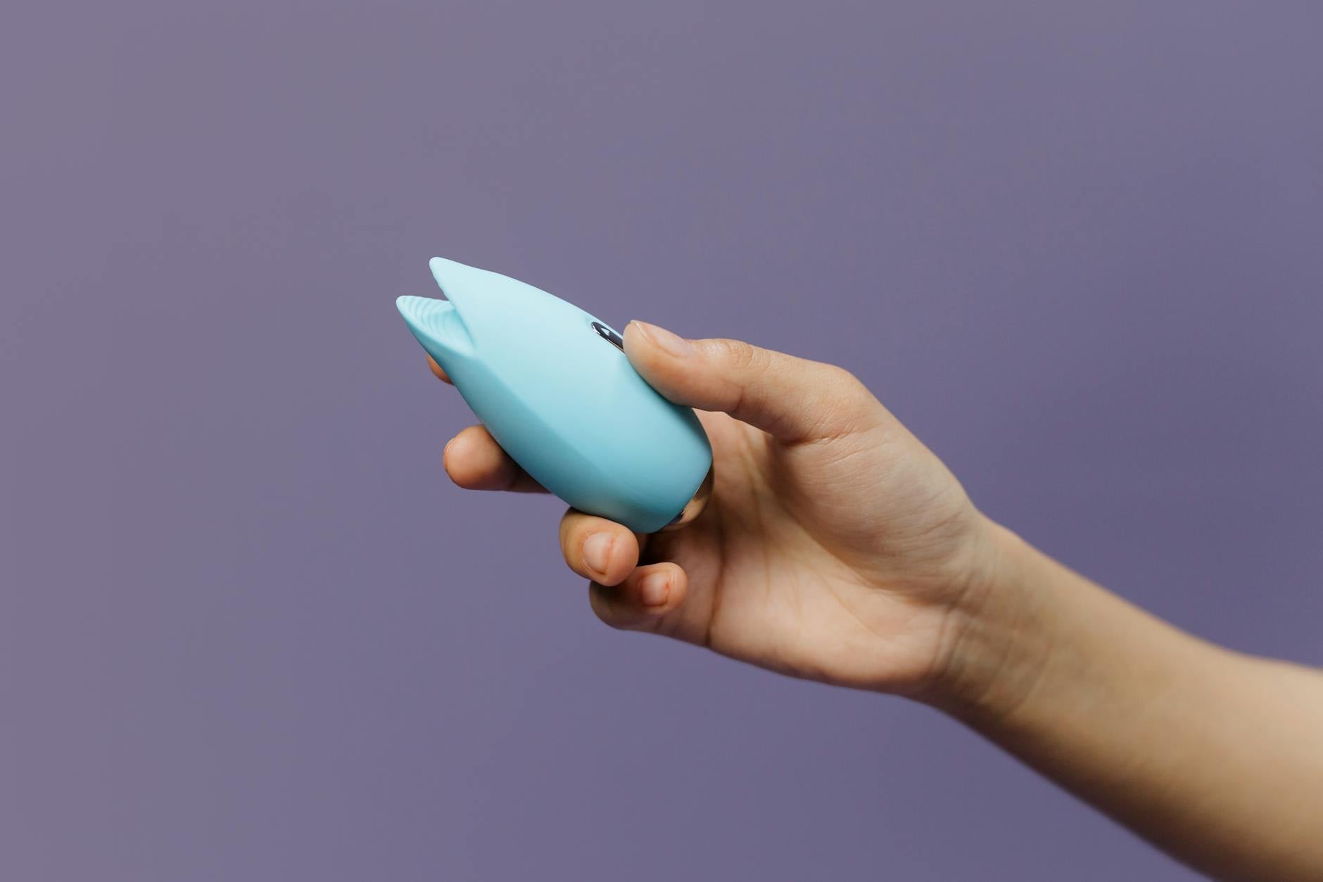 Hands holding a blue clitoral vibrator against a knitted sweater