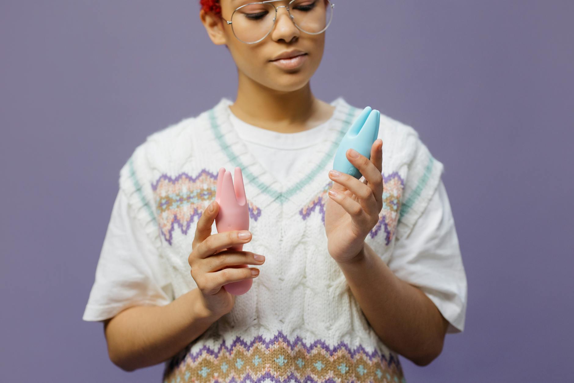Woman holding blue and pink silicone vibrators thoughtfully, exploring pleasure after a long break